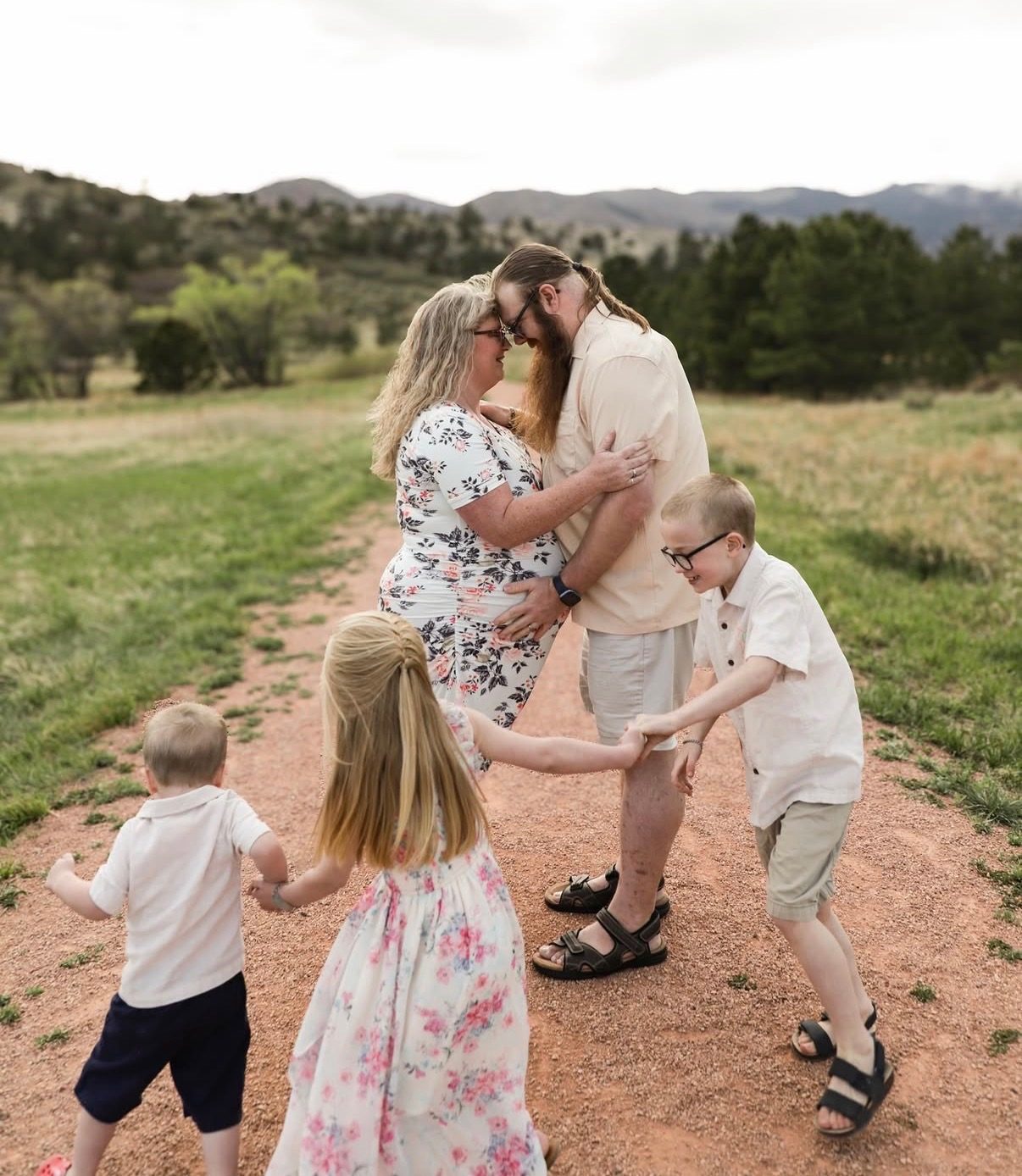 Parents embracing on a dirt path while three children run and hold hands around them.