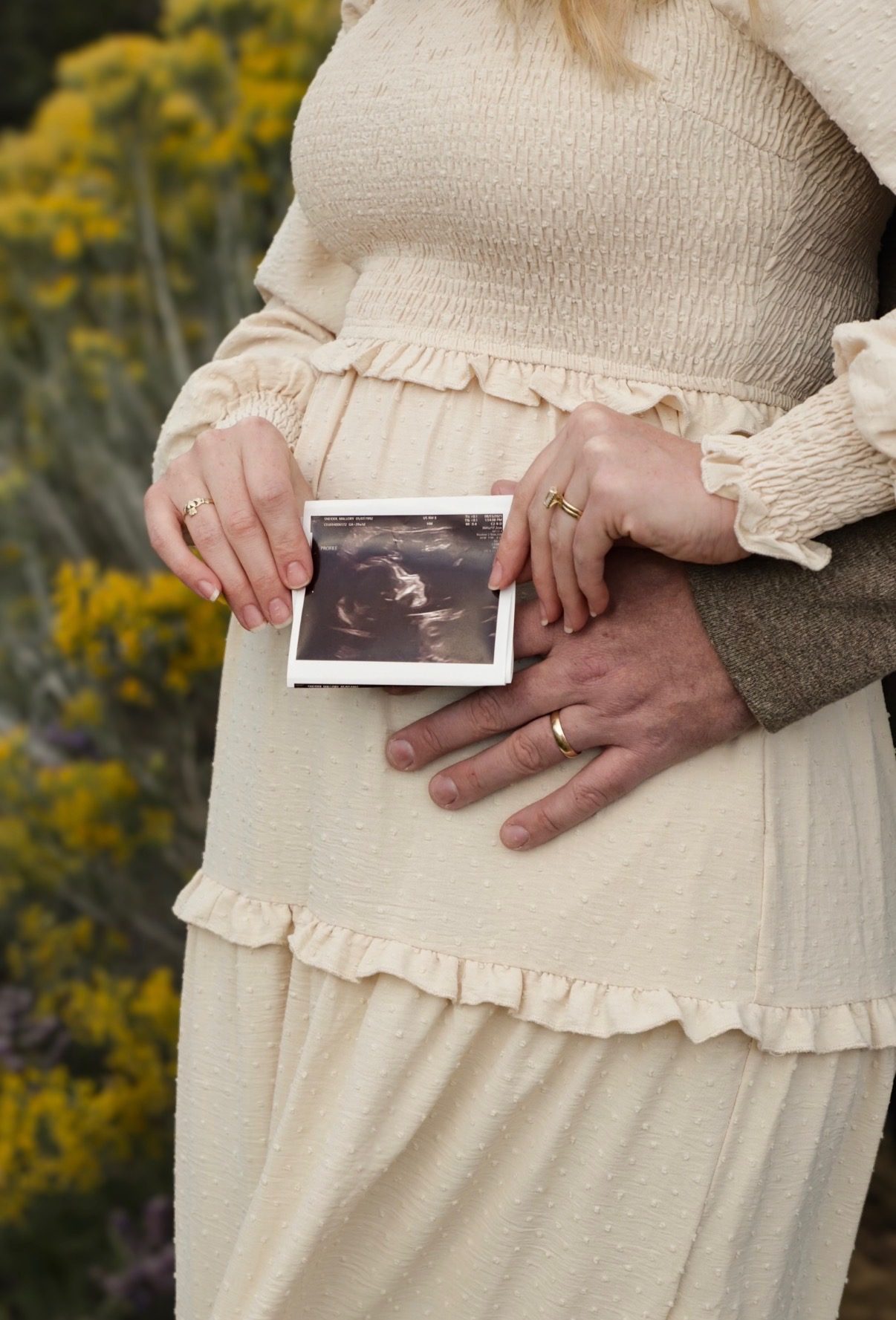 A close-up of an expectant couple's hands holding an ultrasound photo against her bump.