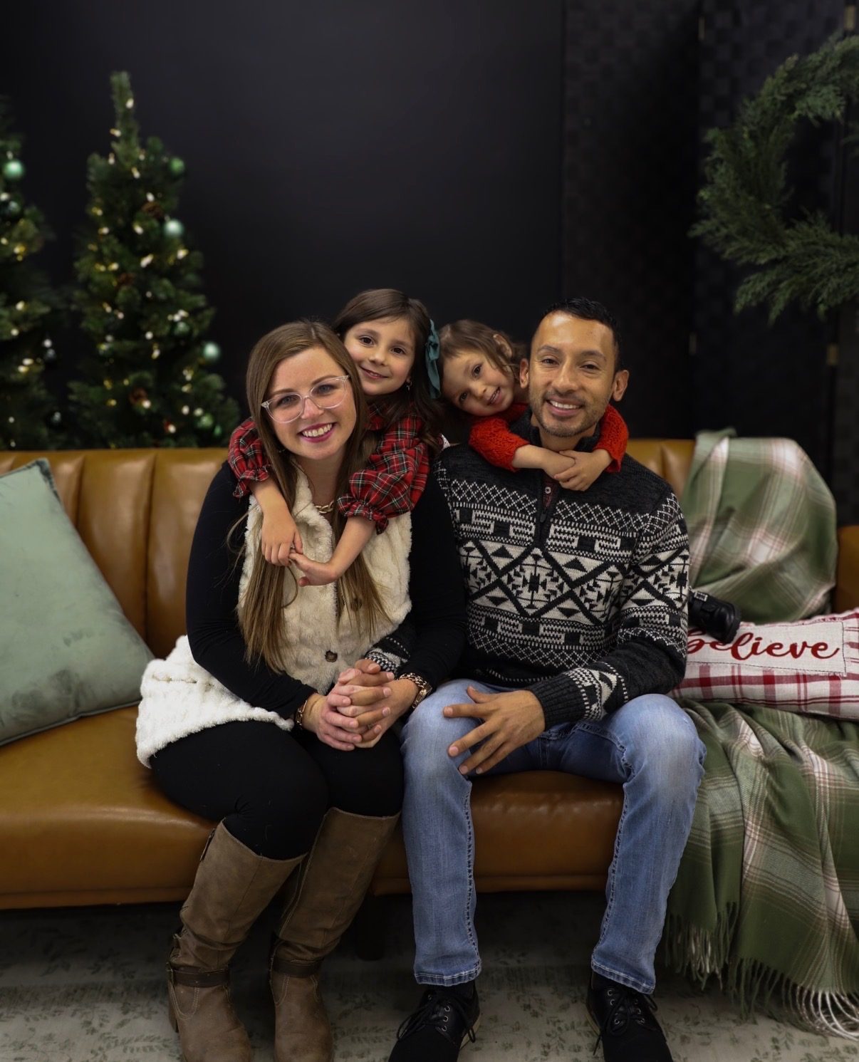 A family of four sitting on a leather sofa beside a decorated Christmas tree.