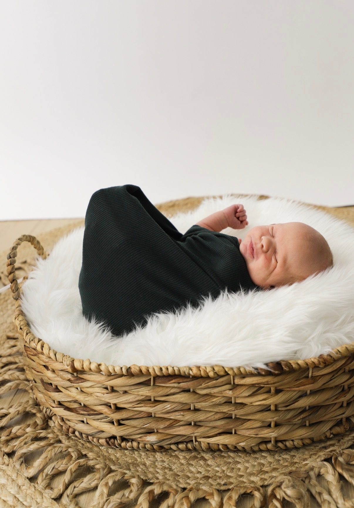A swaddled newborn sleeping in a woven basket lined with white fur.