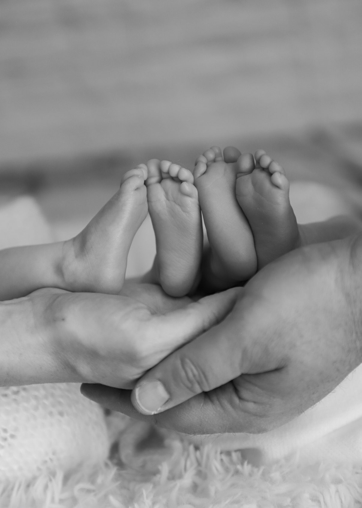 A black and white photograph of a newborn's feet cupped in a parent's hands.